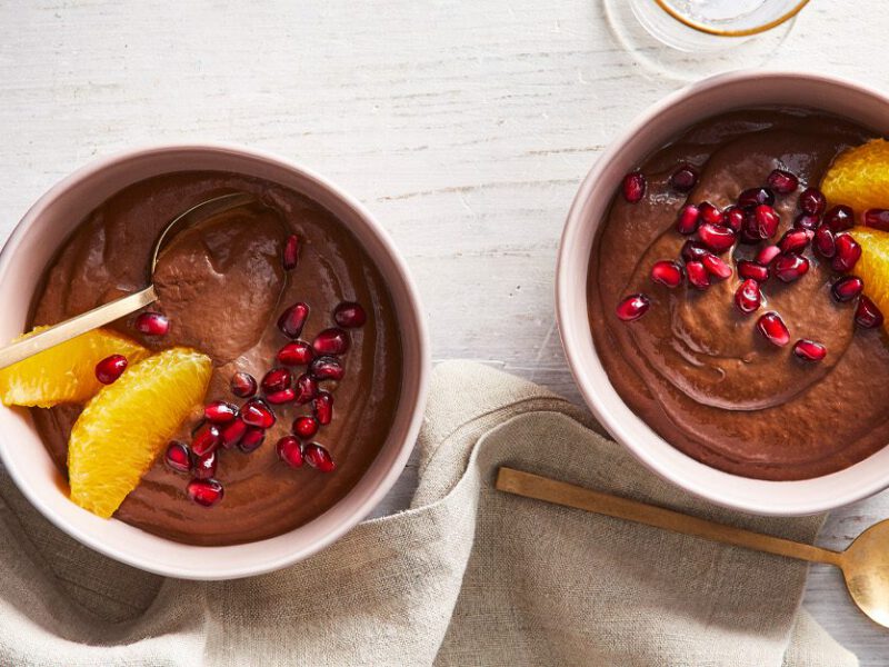 Vegan chocolate avocado pudding in white ramekins sprinkled with pomegranate seeds and orange slices