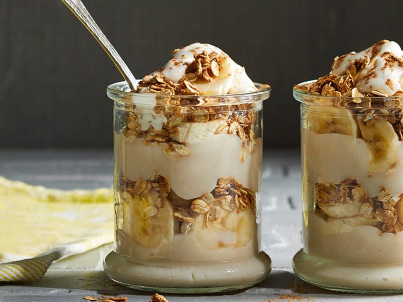 Two vegan banana pudding parfaits in glass jars, showing layers of pudding and vanilla oats