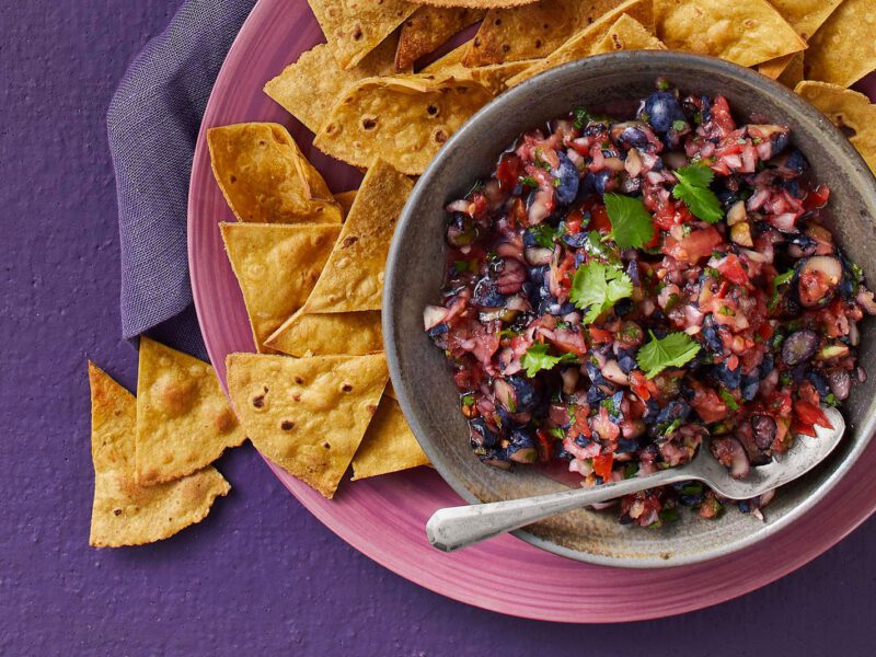 Blueberry salsa with tortilla chips on the side on a purple table