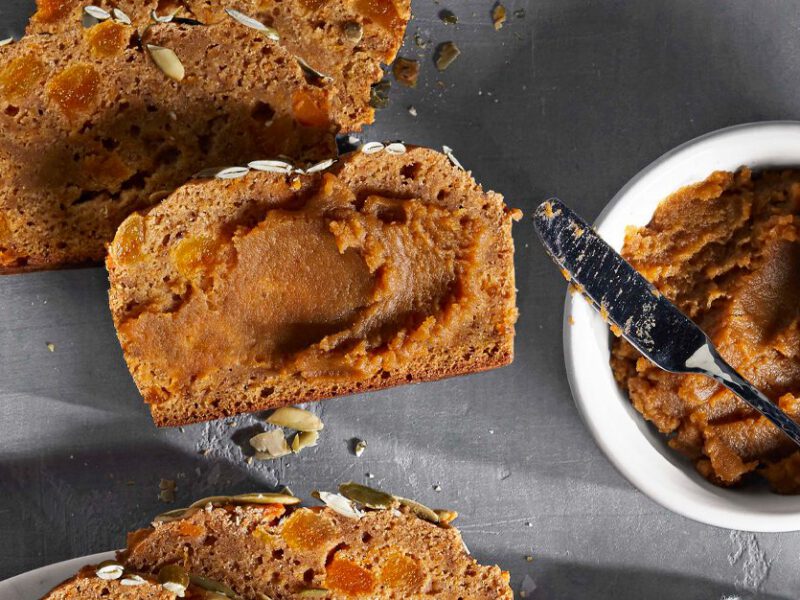 Sweet Potato Butter in a white bowl with a metal knife next to slices of bread slathered in the butter