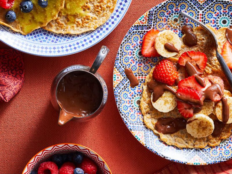 Sweet Moroccan Pancakes with Chocolate Banana Sauce and fresh fruit on a colorful plate and red tablecloth