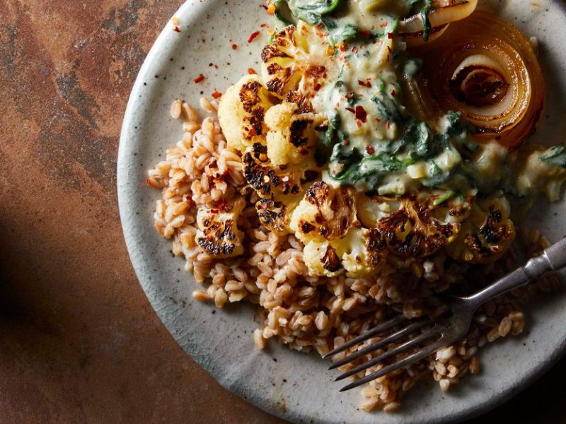 Roasted Cauliflower Steaks with Creamed Spinach on a white plate with a metal fork