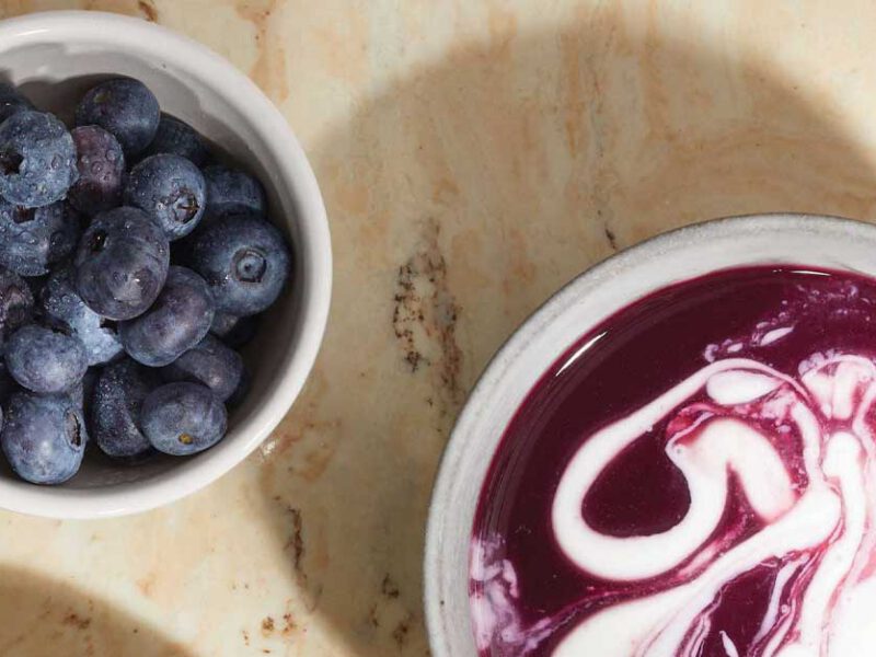 Chilled Blueberry Soup in a white bowl next to a small bowl of fresh blueberries