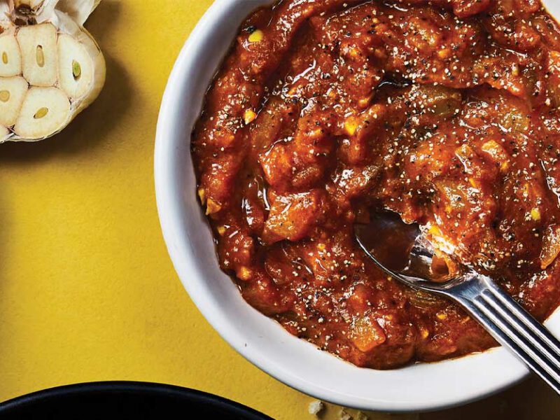 Masala Simmer Sauce in a white bowl next to halved heads of garlic