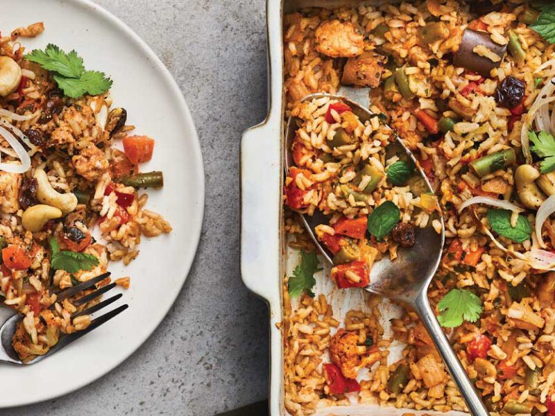 Baked Vegetable Biryani in a casserole dish next to a white plate with a full serving and metal fork