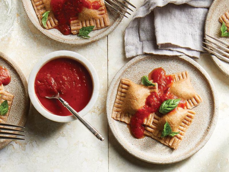 Kale and Sweet Potato–Stuffed Vegan Ravioli on gray ceramic plates topped with marinara sauce and fresh basil