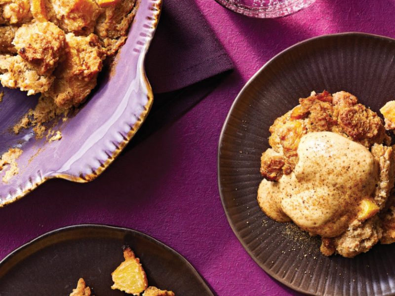 A single serving of Ginger Peach Bread Pudding next to a baking dish against a bright purple tablecloth