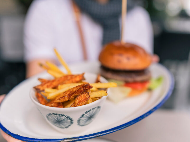 person holding out burger and deep-fried french fries on a plate