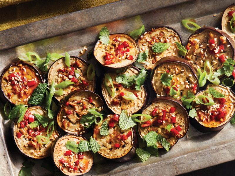 Vietnamese Eggplant with Cashews, Sesame, and Chile cut into 16 rounds, presented in a metal baking tray garnished with fresh mint leaves