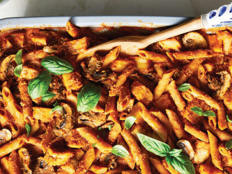 Mediterranean Pasta Bake with Mushrooms and Eggplant in a white and blue casserole dish with a serving spoon