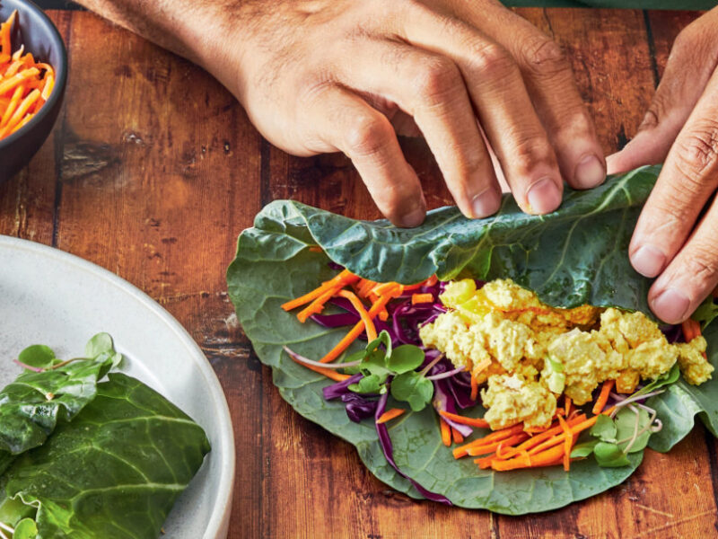 Close up of two hands rolling Dom Thompson's "Egg Salad” Collard Wraps on a wooden counter