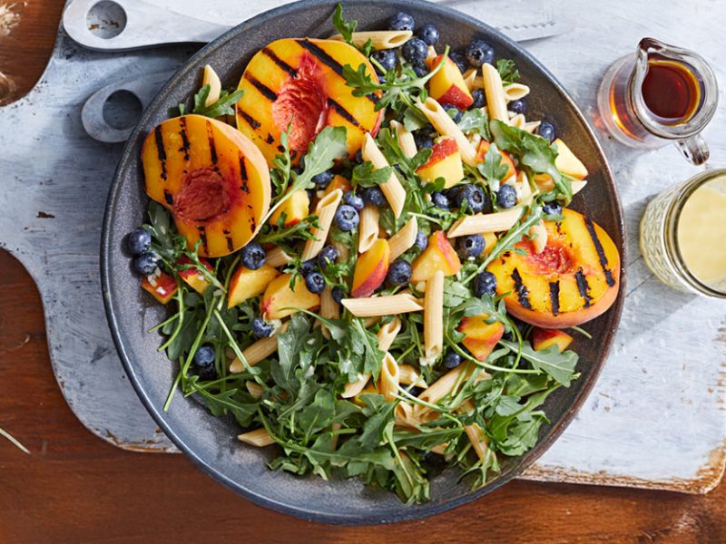 Arugula Peach Blueberry Salad in a bowl on a blue chopping board