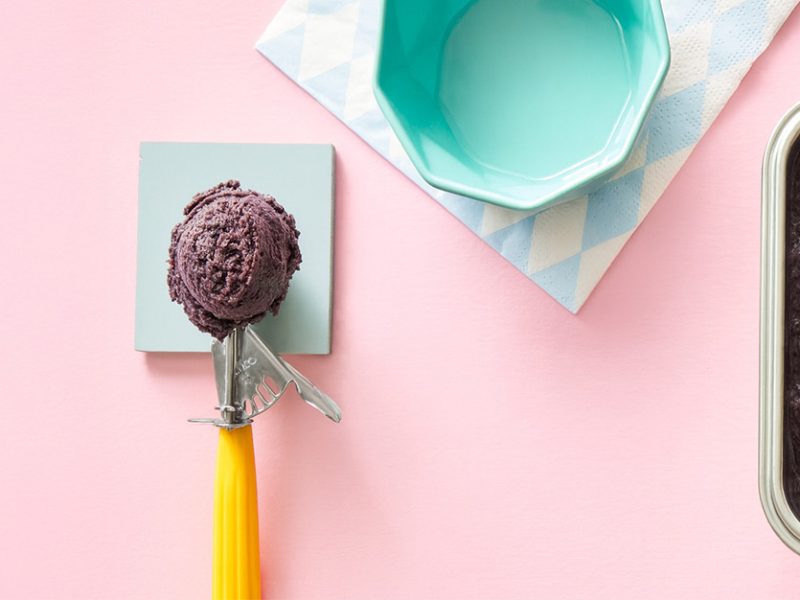 A scoop of Adzuki Bean Nice Cream next to a stainless steel container of the ice cream against a pale pink background