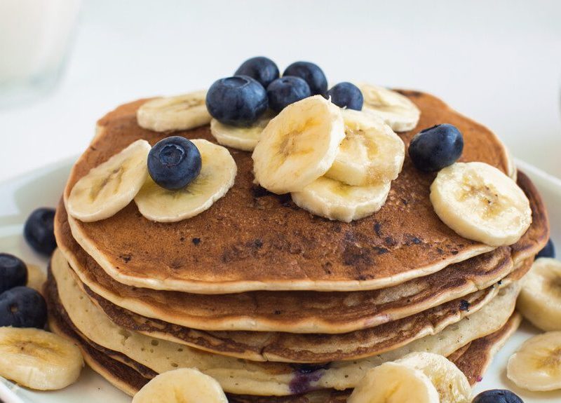 A stack of Banana Pancakes on a plate with fresh blueberries and banana slices