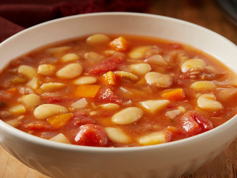 Autumn Lima Bean Stew in a white bowl on a rough wood table with a plate of potato, onion, and cinnamon stick in the background