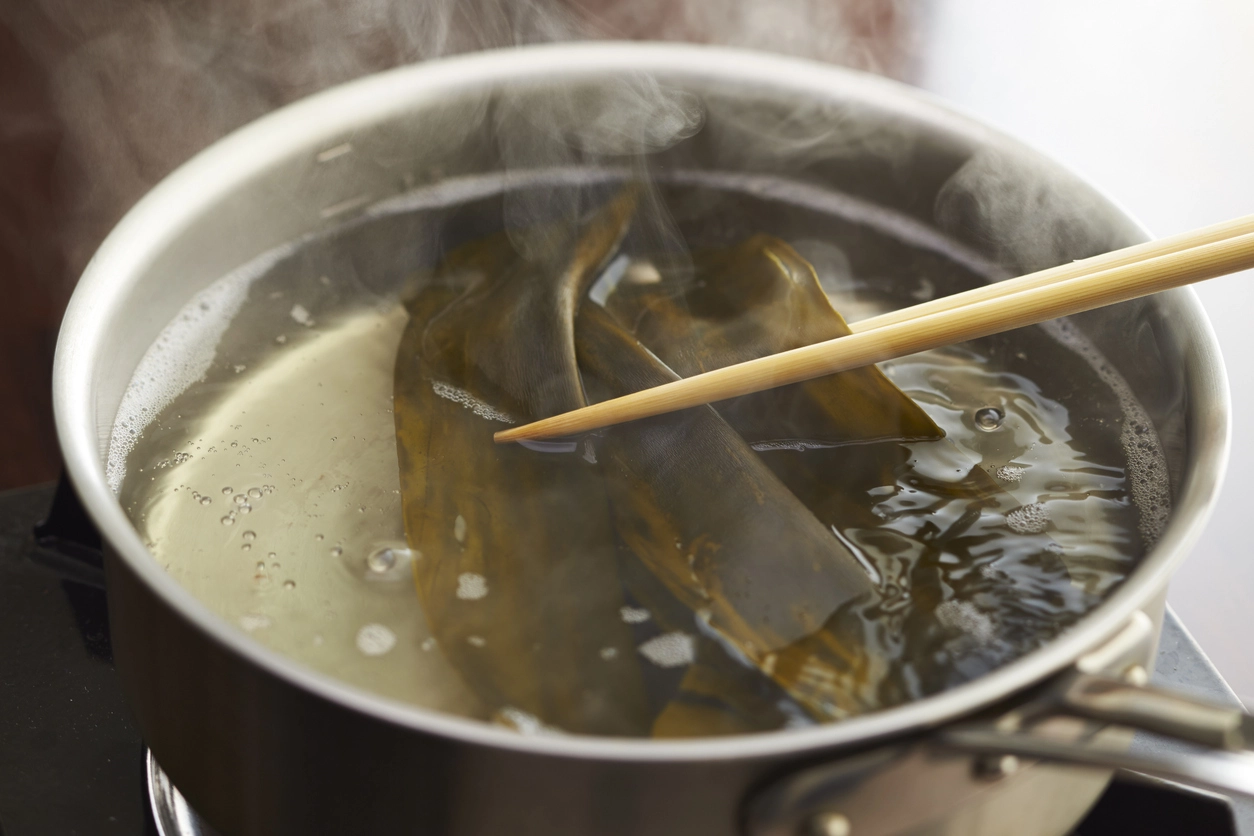 Vegan kombu dashi broth in a pot of water, with chopsticks lifting the dashi out of the pot
